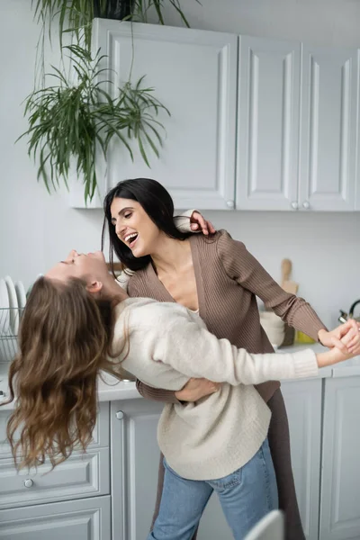 Cheerful lesbian couple in warm clothes dancing in kitchen — Stock Photo