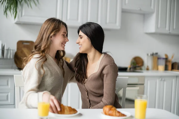 Vista lateral de pareja lesbiana positiva mirándose el uno al otro cerca del desayuno en la cocina - foto de stock