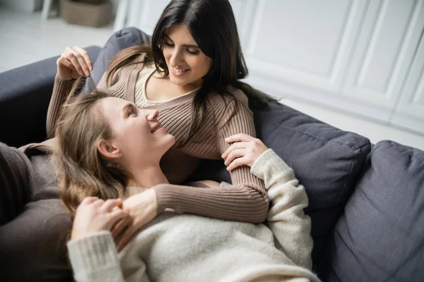 Позитивная лесбийская пара трогает друг друга на диване дома — стоковое фото