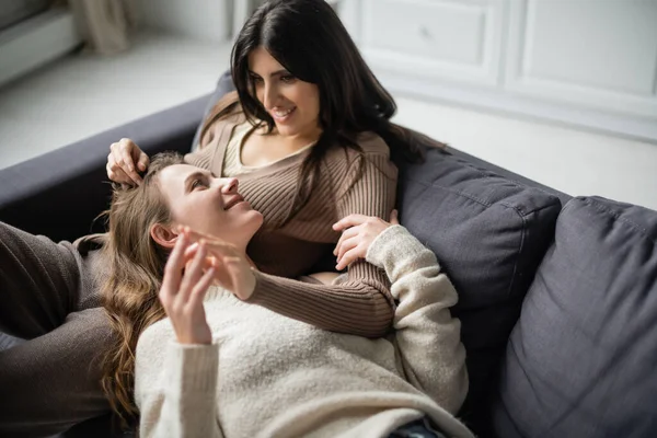 Улыбающаяся лесбиянка трогает руку подружки на диване дома — стоковое фото