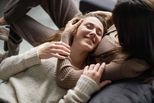 Вид под высоким углом на лесбиянку, трогающую улыбающуюся девушку дома на диване — стоковое фото