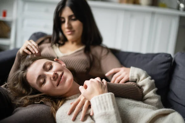 Усміхнена лесбіянка лежить біля розмитої дівчини на дивані — стокове фото