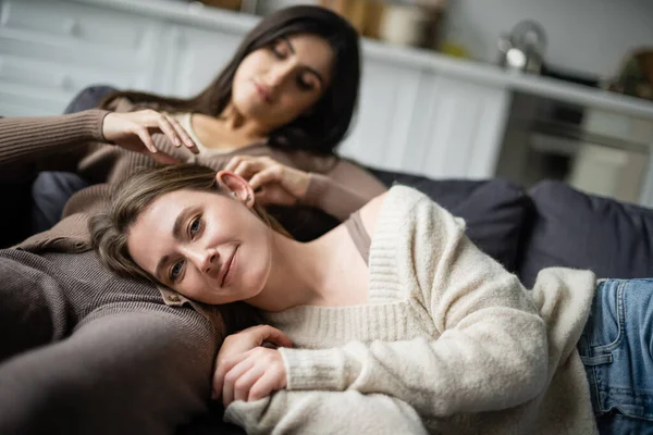 Молодая женщина смотрит в камеру, лежа рядом с размытой девушкой на диване — стоковое фото
