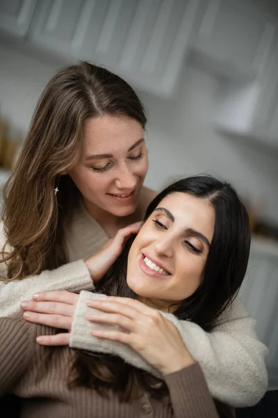Positive woman embracing and looking at girlfriend at home — Stock Photo