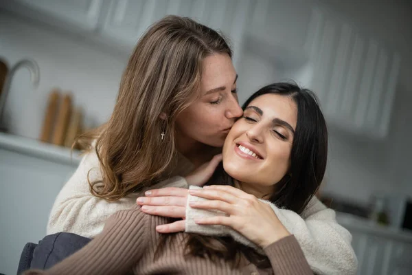 Woman kissing cheerful girlfriend with closed eyes at home — Stock Photo
