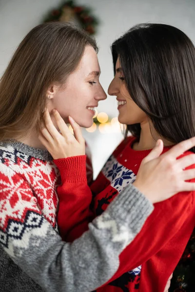 Vue latérale du couple lesbien positif en chandails de Noël se touchant à la maison — Photo de stock