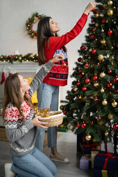 Vue latérale du couple souriant de même sexe décorant l'arbre de Noël dans le salon — Photo de stock