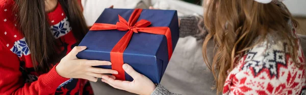 Cropped view of same sex couple in sweaters holding christmas present at home, banner — Stock Photo