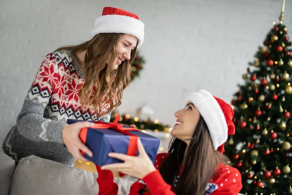 Junge Frau mit Weihnachtsmann beschenkt Freundin bei Silvesterfeier zu Hause — Stockfoto