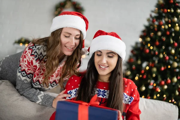 Positivo casal lésbico em presentes de Natal olhando para o presente de ano novo borrado em casa — Fotografia de Stock