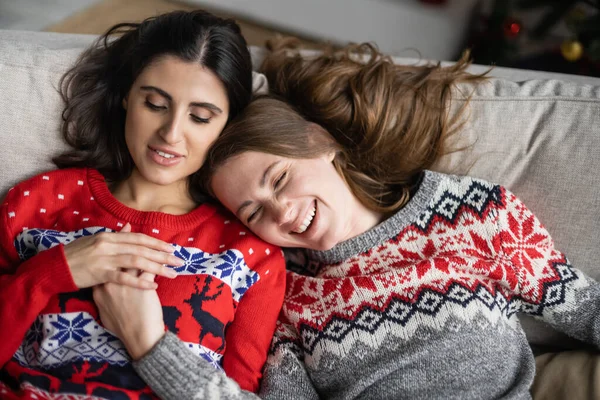 Blick aus der Vogelperspektive auf ein fröhliches lesbisches Paar in Neujahrspullis, das sich zu Hause an den Händen hält — Stockfoto