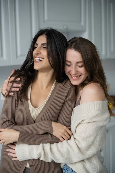 Fröhliche Frau im Pullover umarmt Freundin zu Hause — Stockfoto