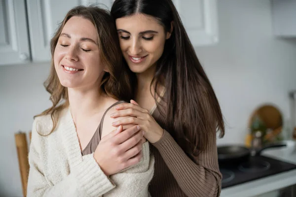 Позитивна жінка торкається плеча дівчини в светрі на кухні — стокове фото