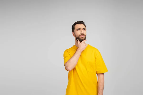 Pensive man in yellow t-shirt touching beard and looking away isolated on grey — Stock Photo