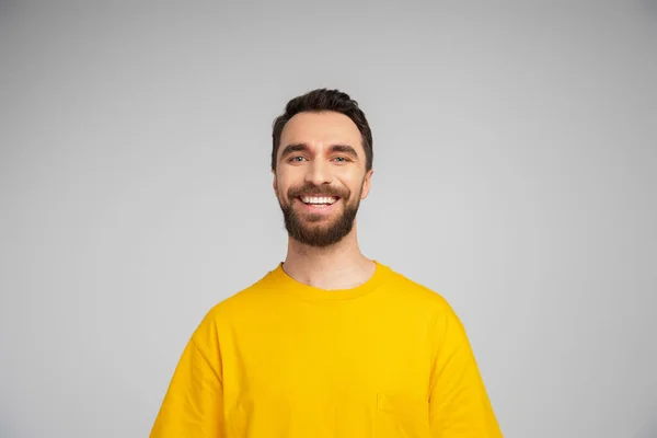 Счастливая брюнетка и бородатый мужчина в желтой футболке, смотрящий на камеру, изолированную на сером — стоковое фото