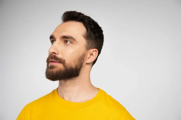 Retrato de morena barbudo hombre en camiseta amarilla mirando hacia otro lado aislado en gris - foto de stock
