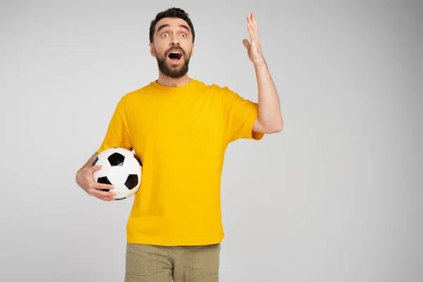 Amazed sports fan with open mouth holding soccer ball and gesturing isolated on grey — Stock Photo