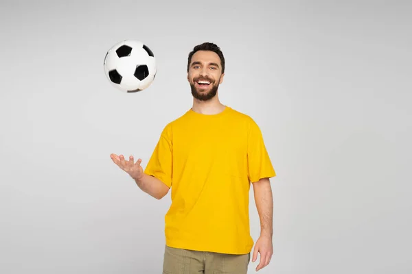 Cheerful sports fan in yellow t-shirt playing with soccer ball isolated on grey — Stock Photo