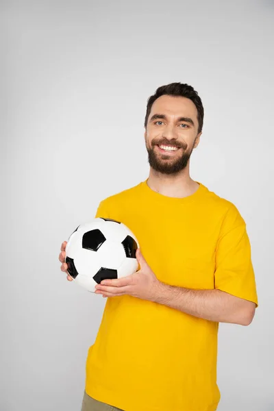 Appassionato di sport barbuto con pallone da calcio sorridente alla fotocamera isolata su grigio — Foto stock