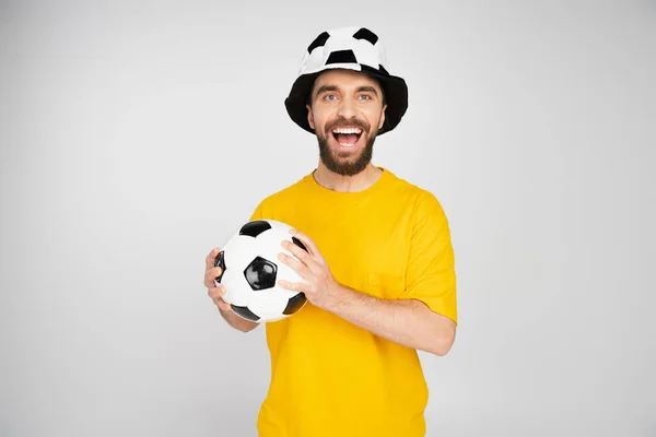 Alegre hombre en fútbol abanico sombrero celebración bola y gritando aislado en gris - foto de stock