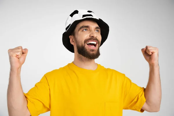 Alegre barbudo hombre en fútbol abanico sombrero mostrando ganar gesto y gritando aislado en gris - foto de stock
