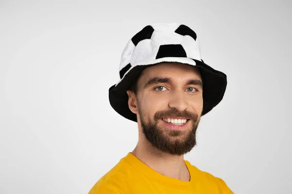 Retrato de hombre barbudo en el sombrero del ventilador de fútbol sonriendo a la cámara aislada en gris - foto de stock