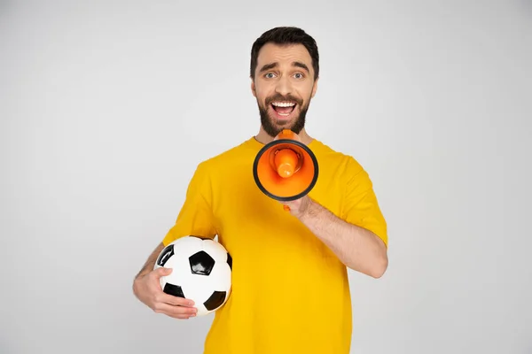 Erstaunt und glücklich Fußballfan hält Fußballball und schreit in Megafon isoliert auf grau — Stockfoto