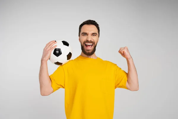 Overjoyed bearded man with soccer ball showing triumph gesture and screaming isolated on grey — Stock Photo