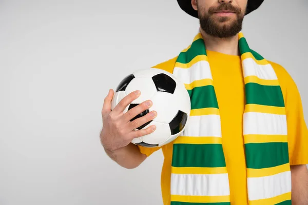 Обрезанный вид бородатого человека в полосатом шарфе, держащего футбольный мяч, изолированный на сером — стоковое фото