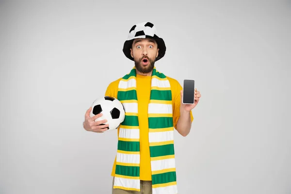 Surprised man in football fan hat showing smartphone with blank screen isolated on grey — Stock Photo