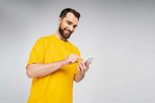 Low angle view of brunette bearded man pointing at mobile phone isolated on grey — Stock Photo