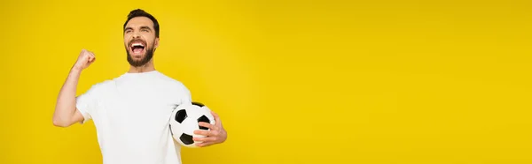 Gritando fã de futebol com bola regozijando e mostrando gesto triunfo isolado em amarelo, banner — Fotografia de Stock