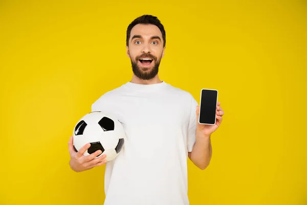 Fan de football étonnant tenant ballon et smartphone avec écran blanc isolé sur jaune — Photo de stock