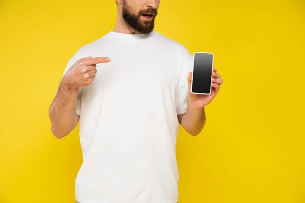 Visão parcial do homem barbudo em camiseta branca apontando para smartphone com tela em branco isolada no amarelo — Fotografia de Stock
