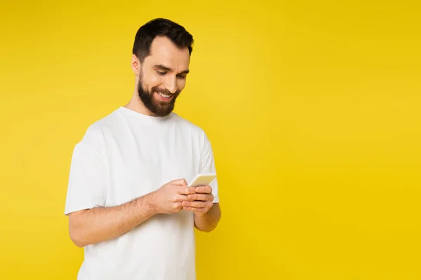 Uomo bruna sorridente con barba chatta sul telefono cellulare isolato sul giallo — Foto stock