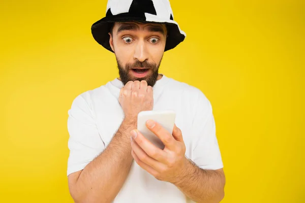 Nervous man in football fan hat watching championship on smartphone isolated on yellow — Stock Photo