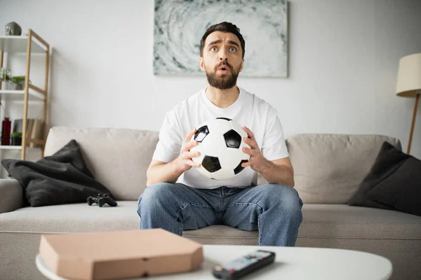 QUIIV, UCRÂNIA - OUTUBRO 21, 2022: homem tenso segurando futebol e assistindo campeonato em casa — Fotografia de Stock