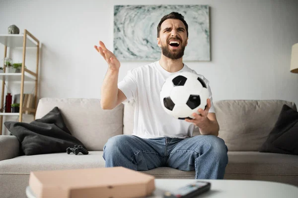QUIIV, UCRÂNIA - OUTUBRO 21, 2022: homem descontente segurando futebol e assistindo campeonato em casa — Fotografia de Stock