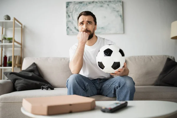 KYIV, UKRAINE - OCTOBER 21, 2022: worried man holding football and watching championship at home — Stock Photo