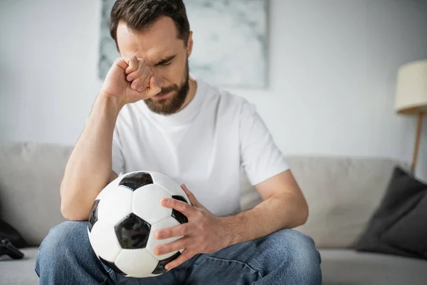 QUIIV, UCRÂNIA - 21 de outubro de 2022: homem chateado segurando futebol depois de assistir campeonato em casa — Fotografia de Stock