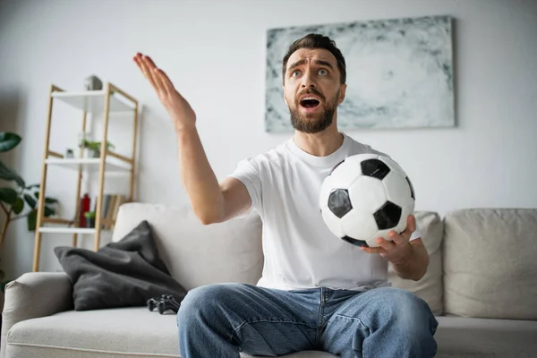 QUIIV, UCRÂNIA - OUTUBRO 21, 2022: homem insatisfeito segurando futebol e assistindo campeonato em casa — Fotografia de Stock