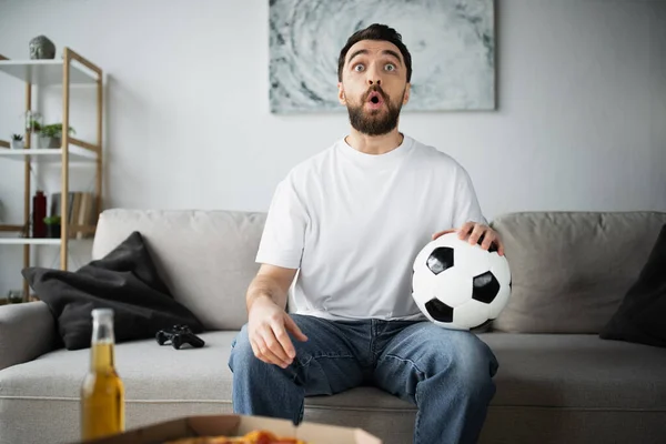 KYIV, UKRAINE - OCTOBER 21, 2022: шокований чоловік тримає футбол і спостерігає за футболом вдома. — стокове фото