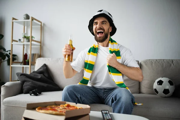 QUIIV, UCRÂNIA - OUTUBRO 21, 2022: Homem espantado de chapéu de fã segurando garrafa de cerveja enquanto assiste ao campeonato — Fotografia de Stock