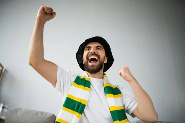 Aufgeregter Mann mit Fanmütze und stilisiertem Schal jubelt und schaut Meisterschaft zu — Stockfoto