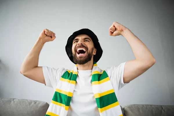 Збуджений чоловік у фан-капелюсі і стиснутий шарф святкування під час перегляду чемпіонату — стокове фото