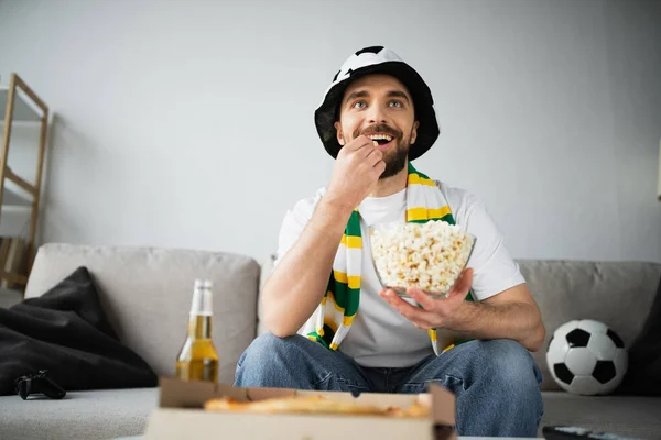 KYIV, UKRAINE - OCTOBER 21, 2022: happy sports fan eating popcorn and watching championship at home — Stock Photo