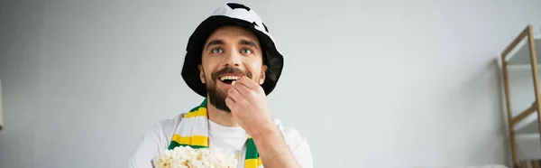 Счастливый спортивный болельщик ест кукурузу и смотрит чемпионат дома, баннер — стоковое фото