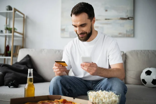 KIEW, UKRAINE - 21. OKTOBER 2022: Glücklicher Mann mit Kreditkarte und Smartphone beim Online-Shopping — Stockfoto