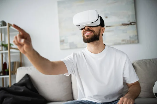 Happy bearded man in vr headset pointing with finger during gaming at home — Stock Photo