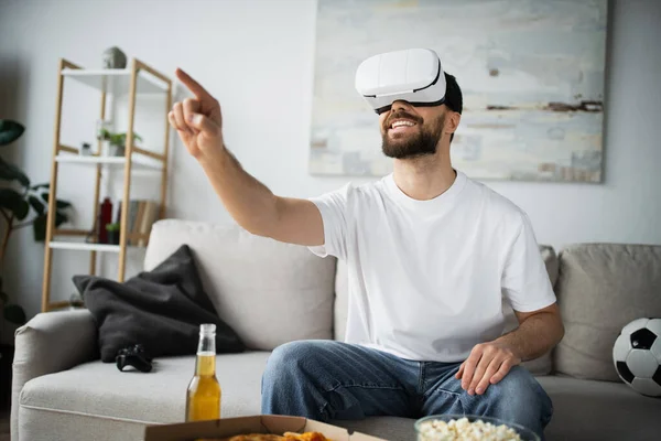 KYIV, UKRAINE - OCTOBER 21, 2022: cheerful man in vr headset pointing with finger during gaming at home — Stock Photo